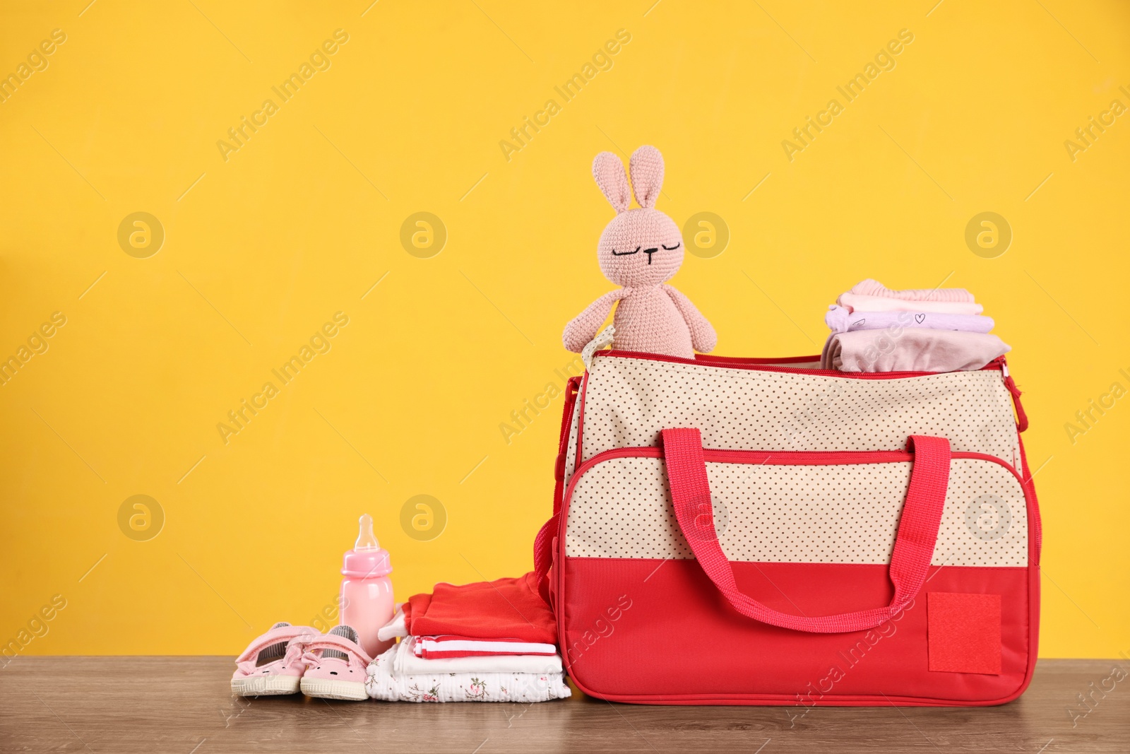 Photo of Mother's bag with baby's stuff on wooden table against orange background. Space for text