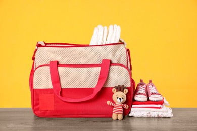 Mother's bag with baby's stuff on wooden table against orange background