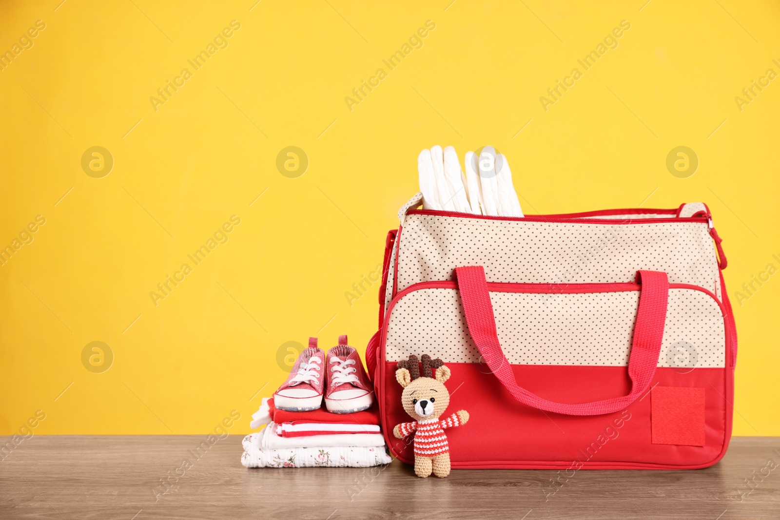 Photo of Mother's bag with baby's stuff on wooden table against orange background. Space for text