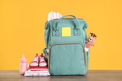 Photo of Mother's bag with baby's stuff on wooden table against orange background