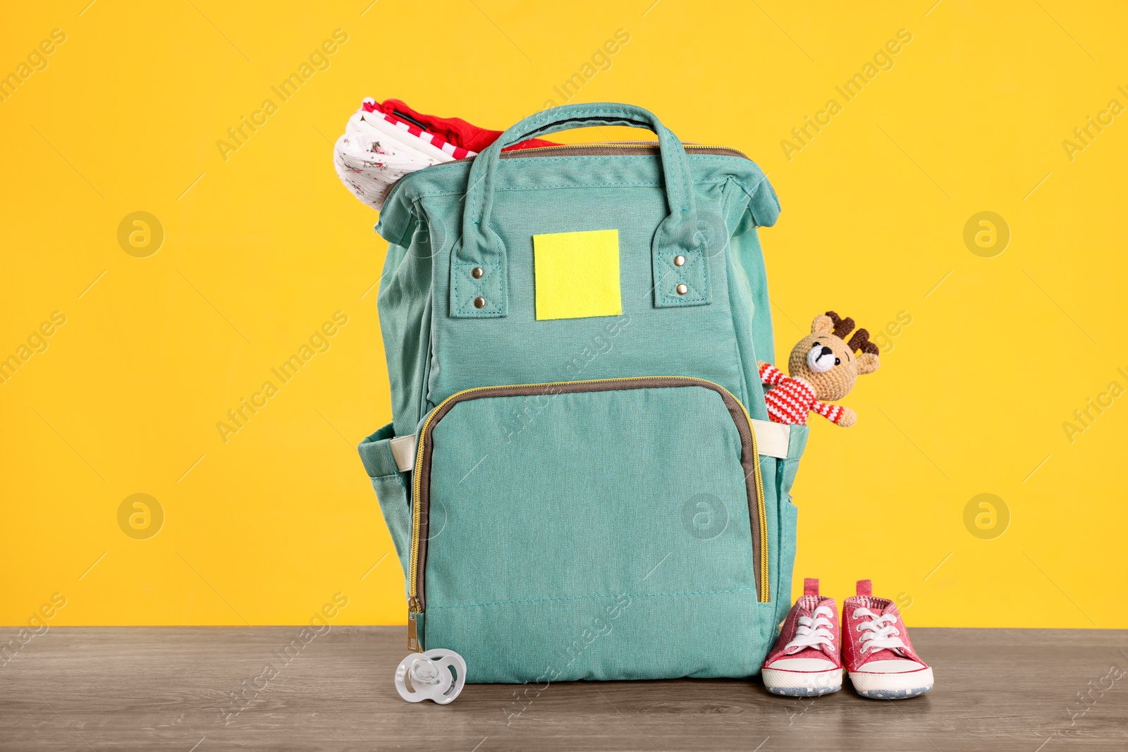 Photo of Mother's bag with baby's stuff on wooden table against orange background