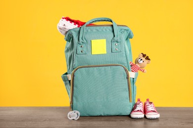 Mother's bag with baby's stuff on wooden table against orange background