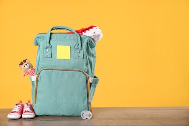 Mother's bag with baby's stuff on wooden table against orange background. Space for text