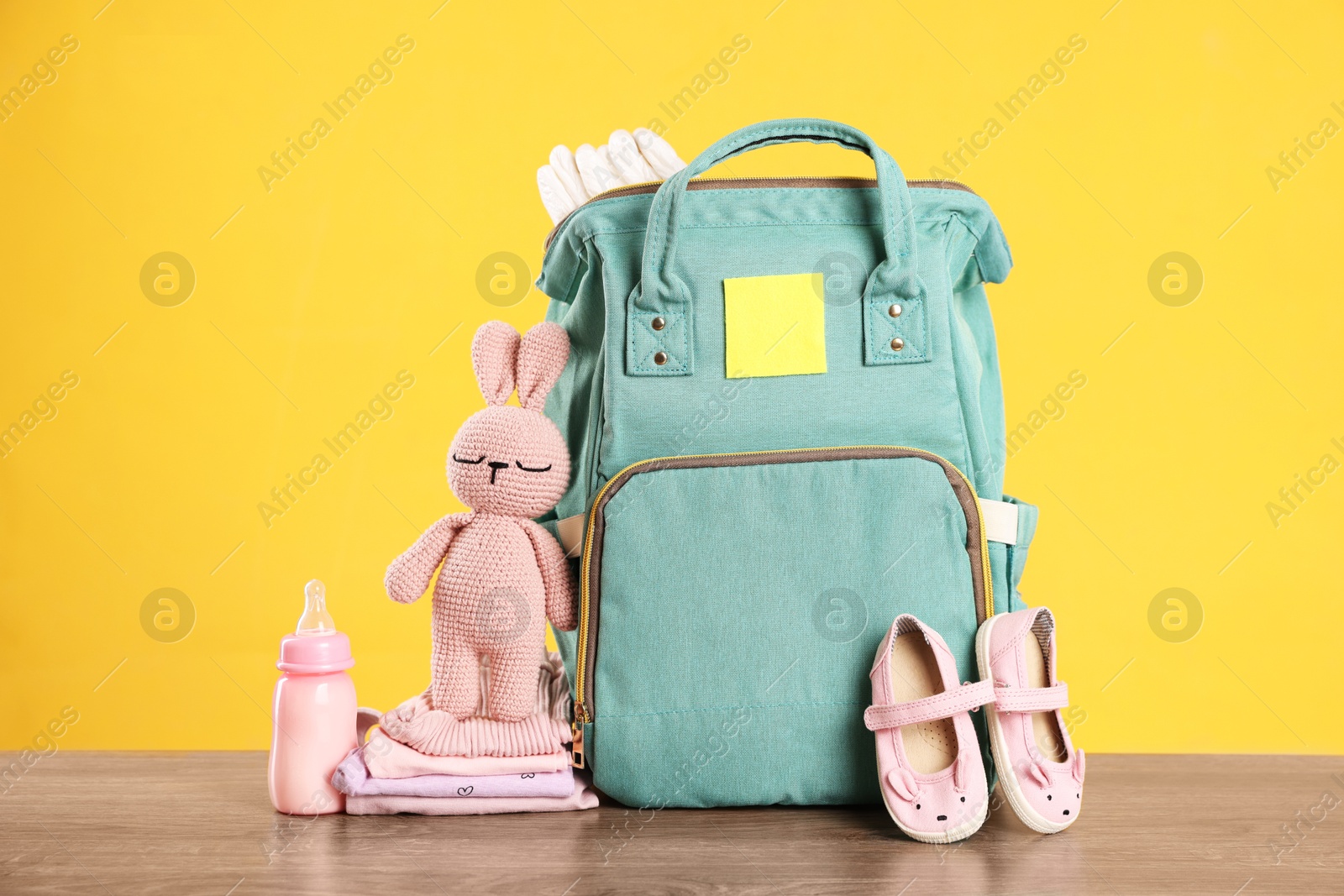 Photo of Mother's bag with baby's stuff on wooden table against orange background