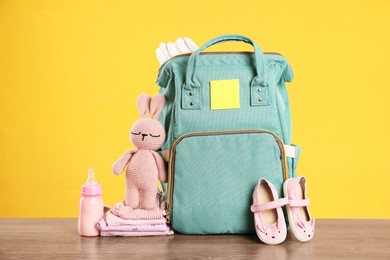 Mother's bag with baby's stuff on wooden table against orange background