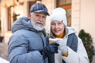 Happy elderly couple with paper cups on city street