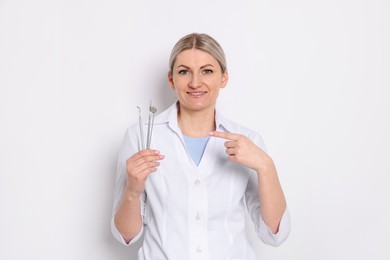 Professional dentist pointing at tools on white background