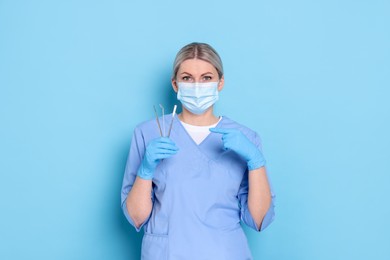 Professional dentist pointing at tools on light blue background