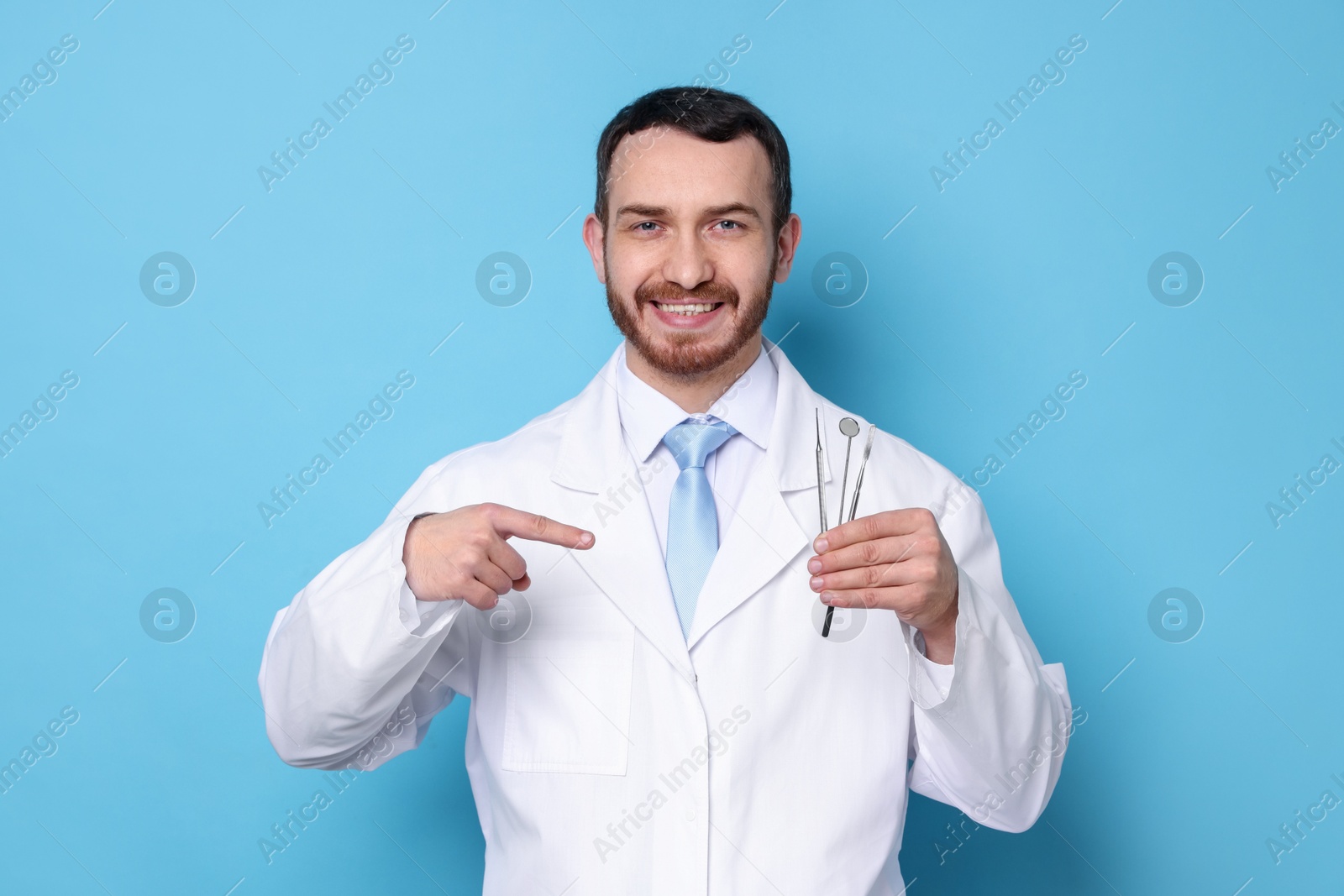 Photo of Professional dentist pointing at tools on light blue background