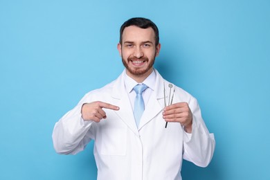 Professional dentist pointing at tools on light blue background