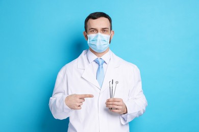 Professional dentist pointing at tools on light blue background