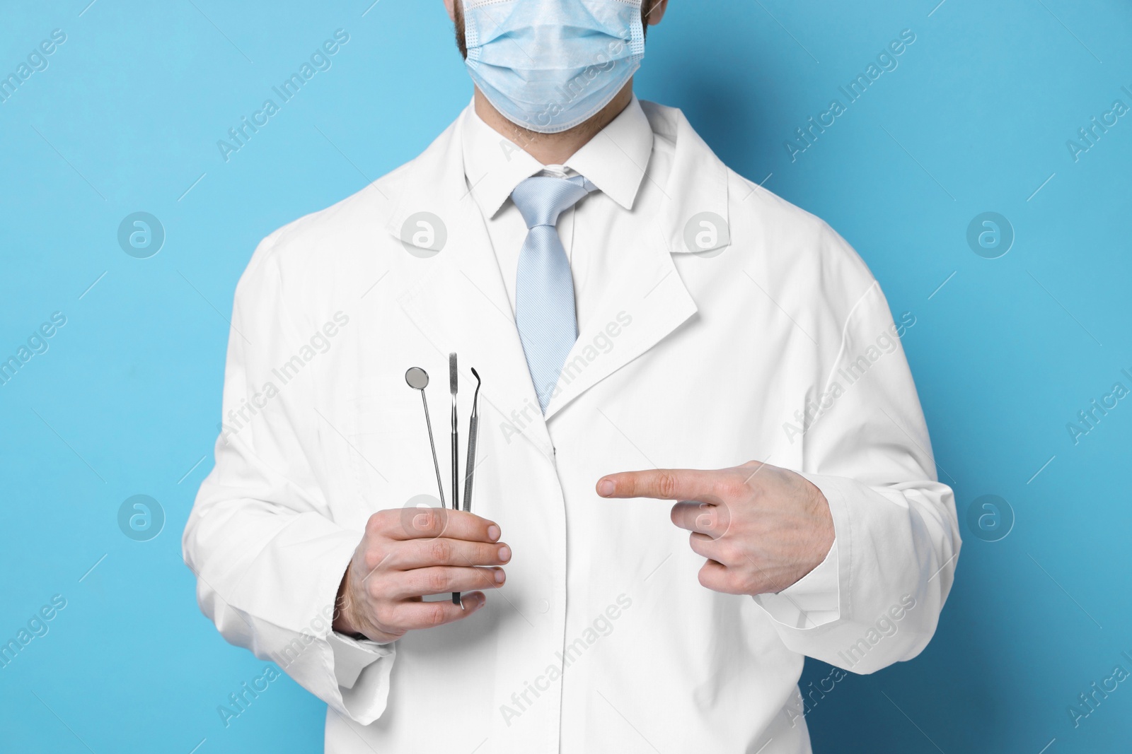 Photo of Professional dentist pointing at tools on light blue background, closeup