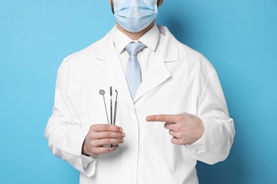 Professional dentist pointing at tools on light blue background, closeup