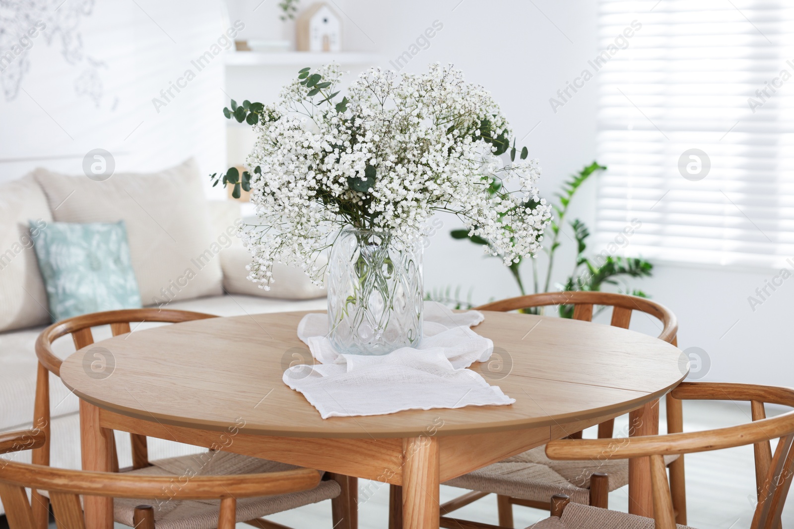 Bouquet of beautiful gypsophila flowers and eucalyptus branches in vase on dinner table indoors Photo of Bouquet of beautiful gypsophila flowers and eucalyptus branches in vase on dinner table indoors