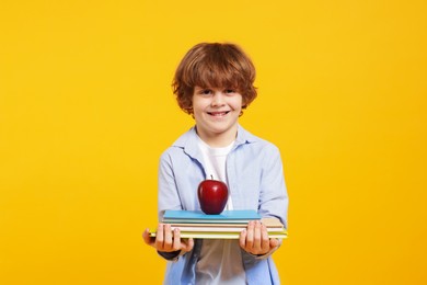 Photo of Cute little boy with books and apple on orange background