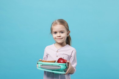 Cute little girl with lunch box on light blue background