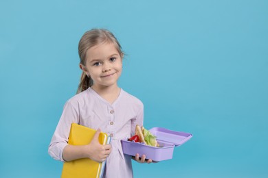 Photo of Cute little girl with lunch box and books on light blue background. Space for text