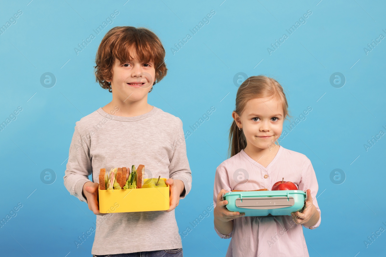 Photo of Cute little children with lunch boxes on light blue background