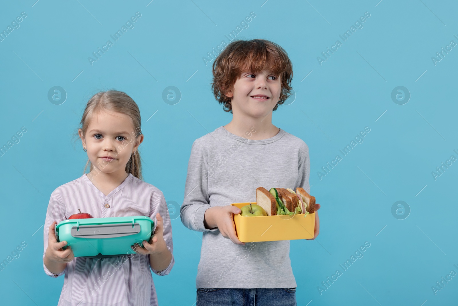 Photo of Cute little children with lunch boxes on light blue background