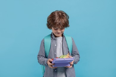 Cute little boy with lunch box on light blue background