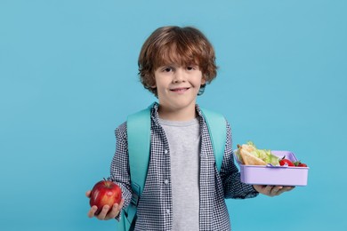 Photo of Cute little boy with lunch box and apple on light blue background