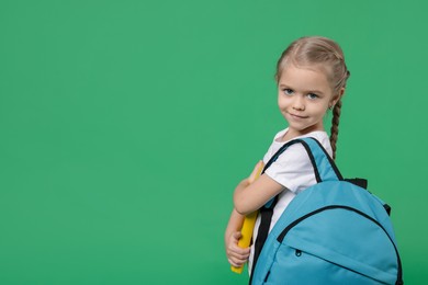 Cute little girl with backpack and book on green background. Space for text