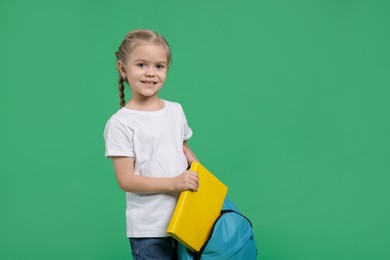 Cute little girl with backpack and book on green background. Space for text