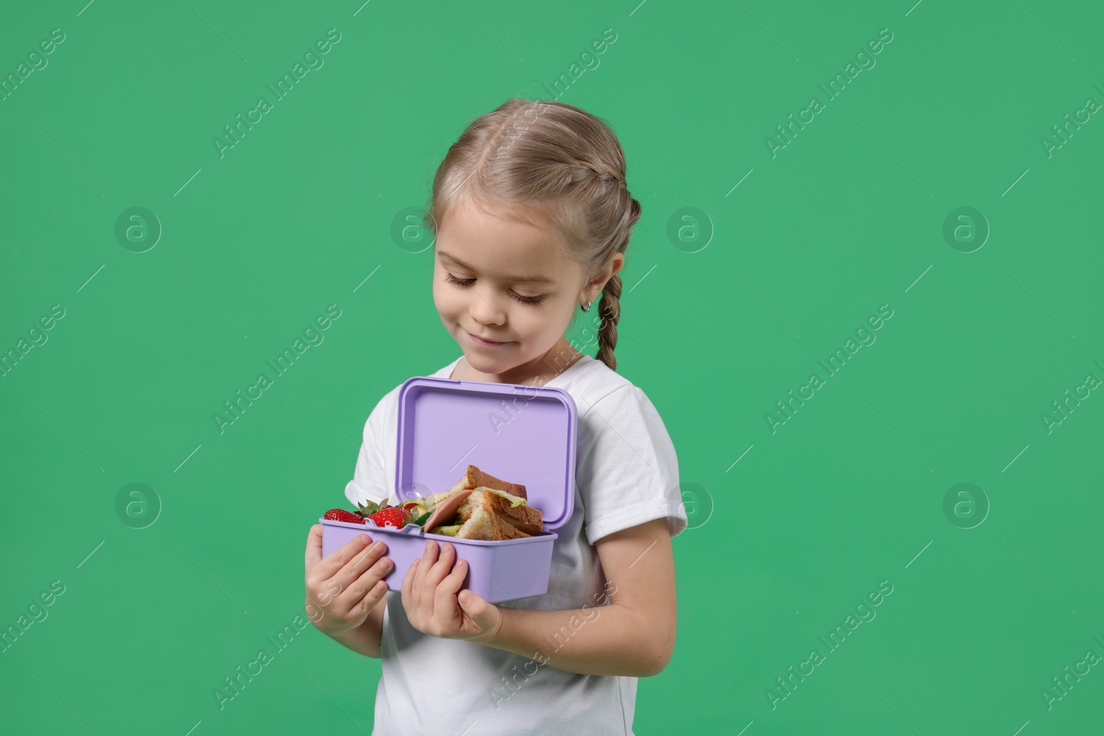 Photo of Cute little girl with lunch box on green background