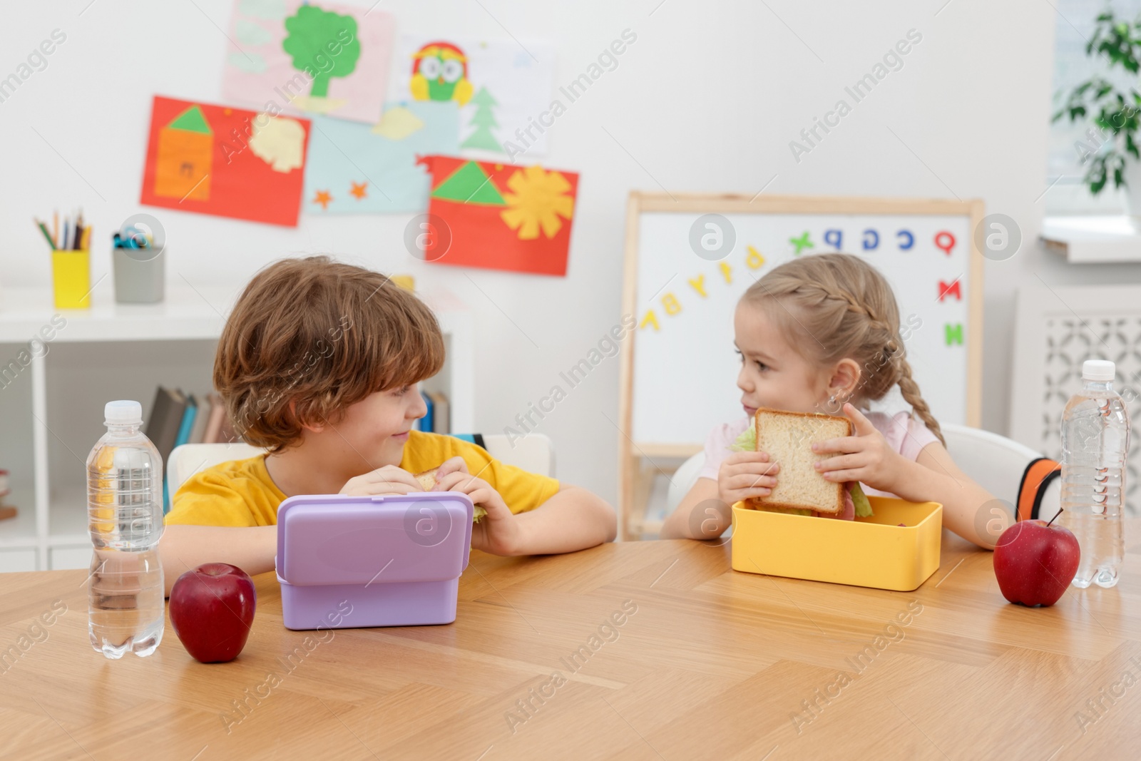 Photo of Cute little children eating lunch at wooden table in school