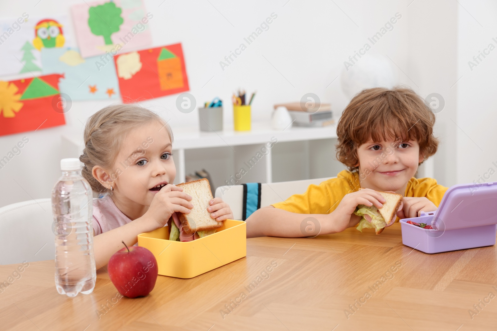 Photo of Cute little children eating lunch at wooden table in school