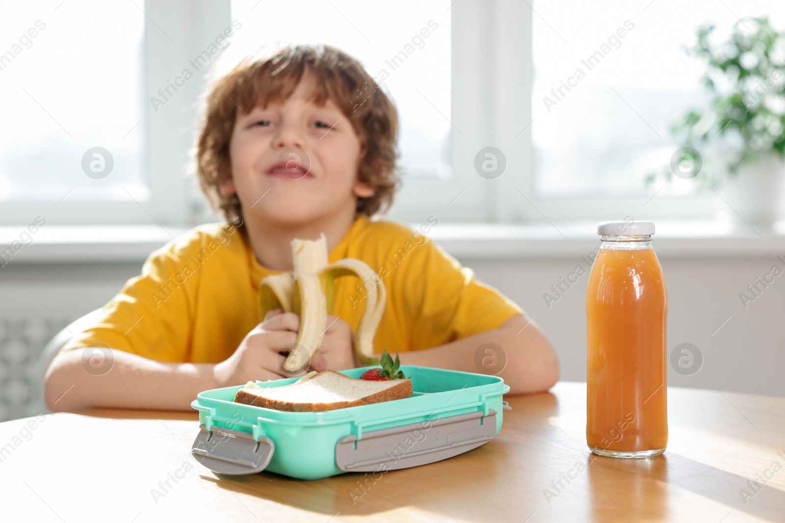 Photo of Cute little boy eating lunch at wooden table in school, selective focus