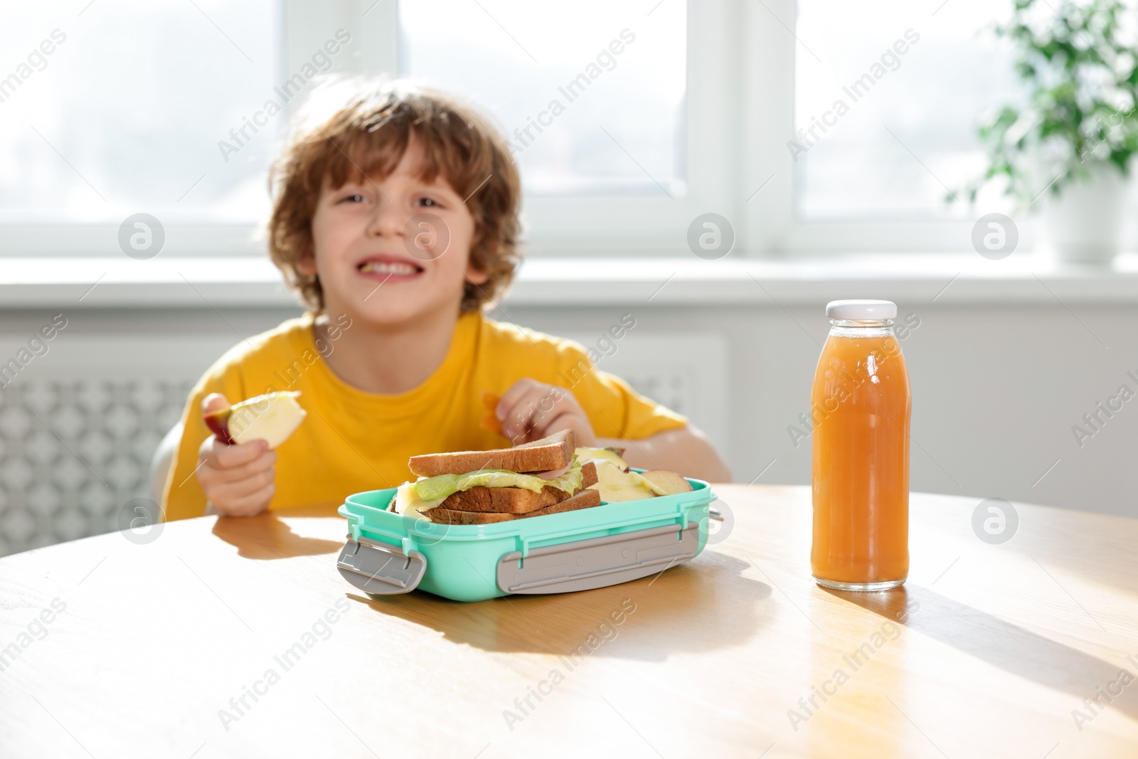 Photo of Cute little boy eating lunch at wooden table in school