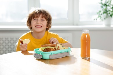 Cute little boy eating lunch at wooden table in school