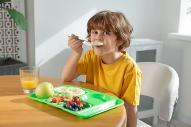 Photo of Cute little boy eating lunch at wooden table in school