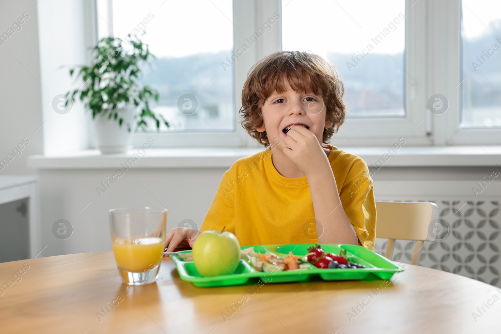 Photo of Cute little boy eating lunch at wooden table in school