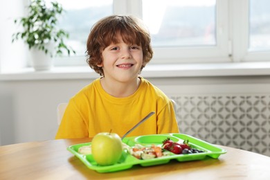 Cute little boy eating lunch at wooden table in school