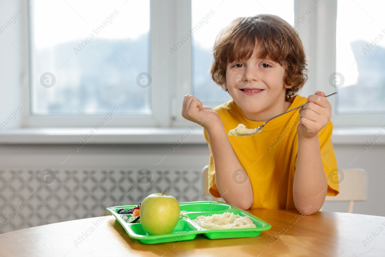 Photo of Cute little boy eating lunch at wooden table in school. Space for text