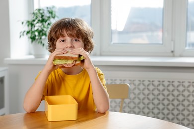 Photo of Cute little boy eating sandwich at wooden table in school. Space for text