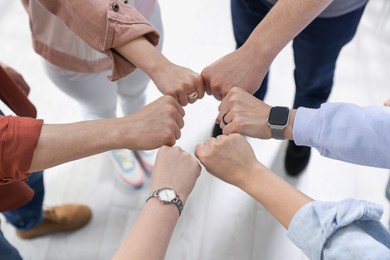 Photo of Unity concept. People holding fists together indoors, above view