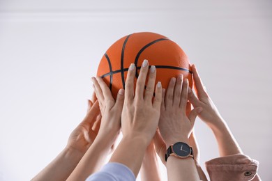 Photo of Unity concept. People holding basketball ball together indoors, closeup