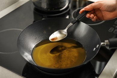 Photo of Woman holding spoon over frying pan with used cooking oil at stove, closeup