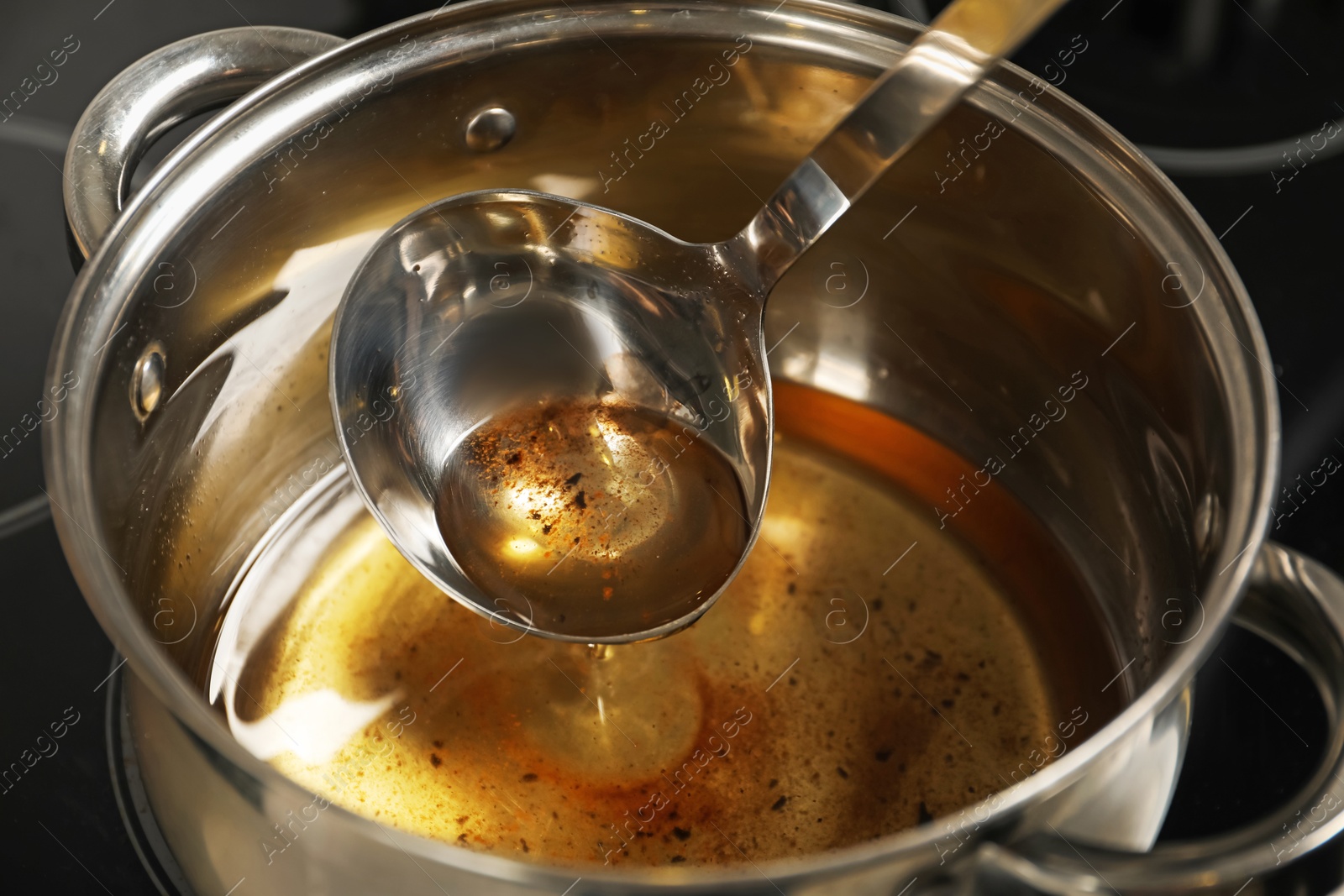 Photo of Pouring used cooking oil from ladle into saucepan, closeup