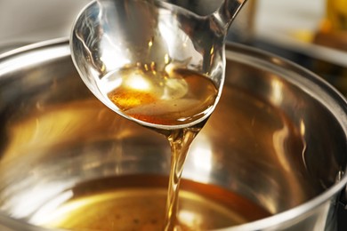 Photo of Pouring used cooking oil from ladle into saucepan, closeup