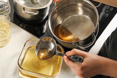 Photo of Woman pouring used cooking oil at white countertop, closeup