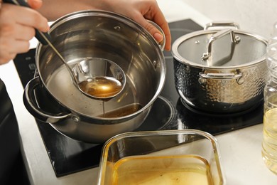 Photo of Woman pouring used cooking oil at white countertop, closeup