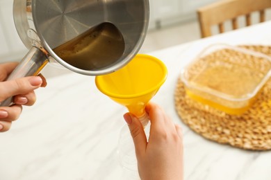 Photo of Woman pouring used cooking oil into bottle through funnel in kitchen, closeup