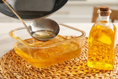 Photo of Pouring used cooking oil into glass container at white table, closeup