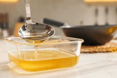 Photo of Pouring used cooking oil into glass container at white marble table, closeup