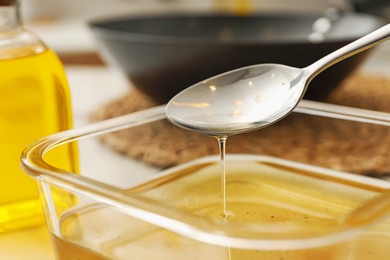 Photo of Pouring used cooking oil into glass container at white table, closeup