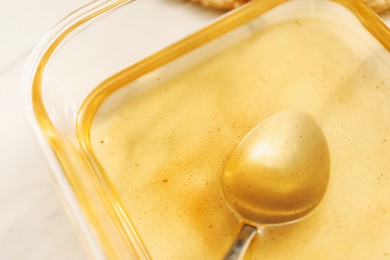 Photo of Used cooking oil and spoon in glass container on white table, closeup